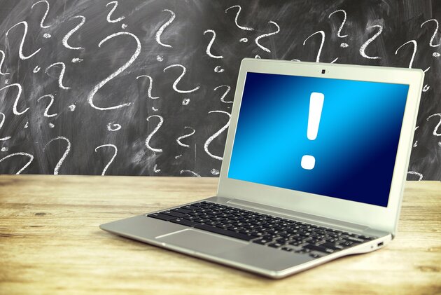 Laptop with exclamation mark in front of blackbord with many question marks.
