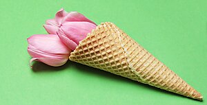 Glasstrut med rosa blommor i som ligger på grön yta.
