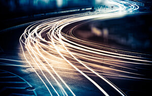 Foto på bilgata på natten, tagit med lång slutartid så strålkastarna bildar streck som följer gatan